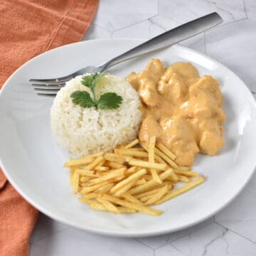 Brazilian chicken stroganoff on a white plate, served with white rice and potato sticks.