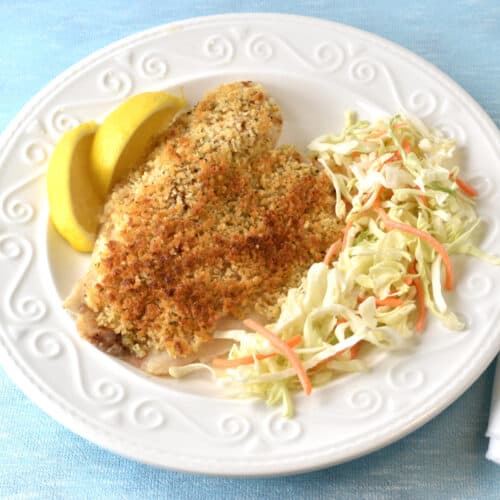 Tilapia with a Parmesan Panko crust on a white plate with salad and lemon wedges.