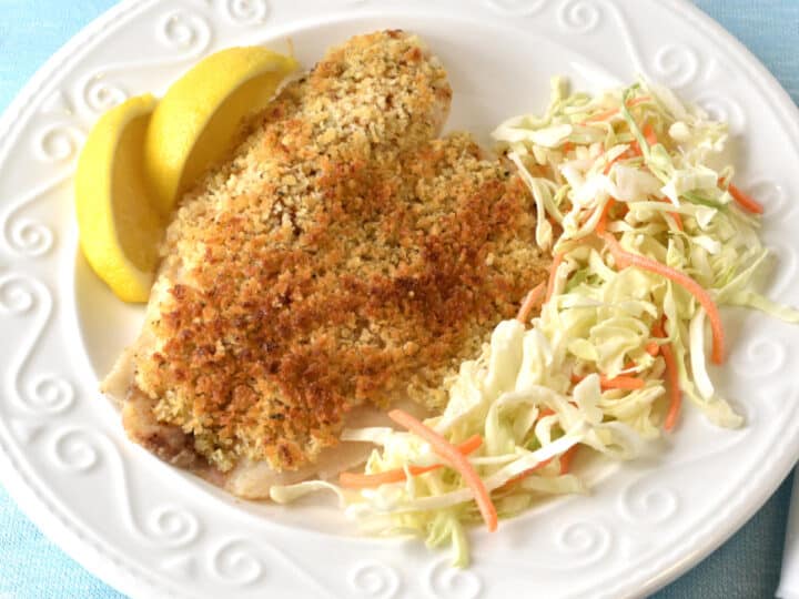 Tilapia with a Parmesan Panko crust on a white plate with salad and lemon wedges.