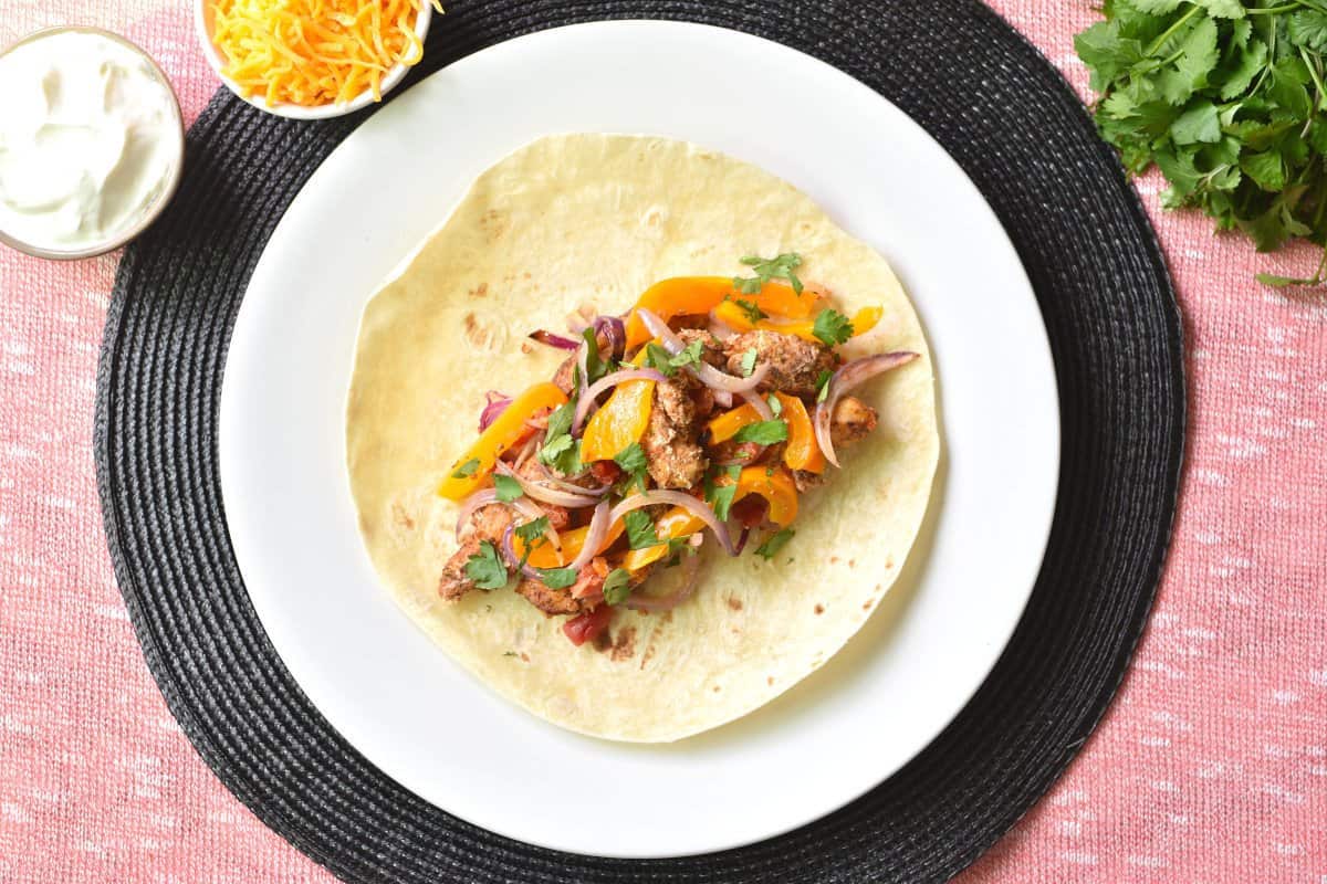 chicken fajitas with yellow bell pepper and red onion on a tortilla