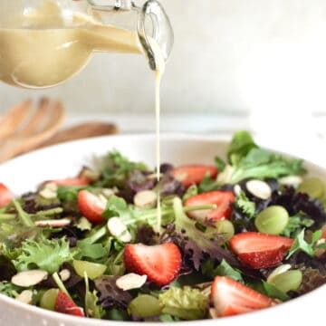 Asian Salad dressing being poured over a salad with strawberries, green grapes and almonds