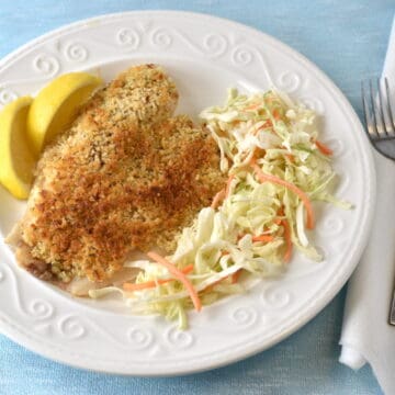Baked tilapia fillet on a white plate with salad and lemon wedges