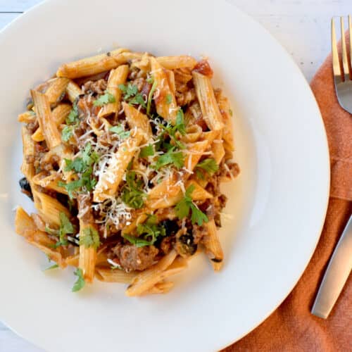 Penne pasta with ground beef, black olives, cilantro and salsa on a white plate.