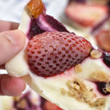 Frozen Yogurt bark. Hand holding it. Topped with strawberry, jam and granola