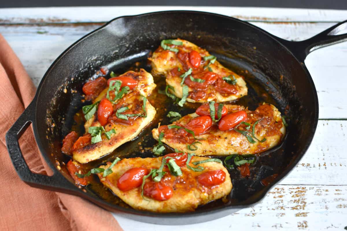 pan seared chicken breasts with grape tomatoes and basil in a iron skillet