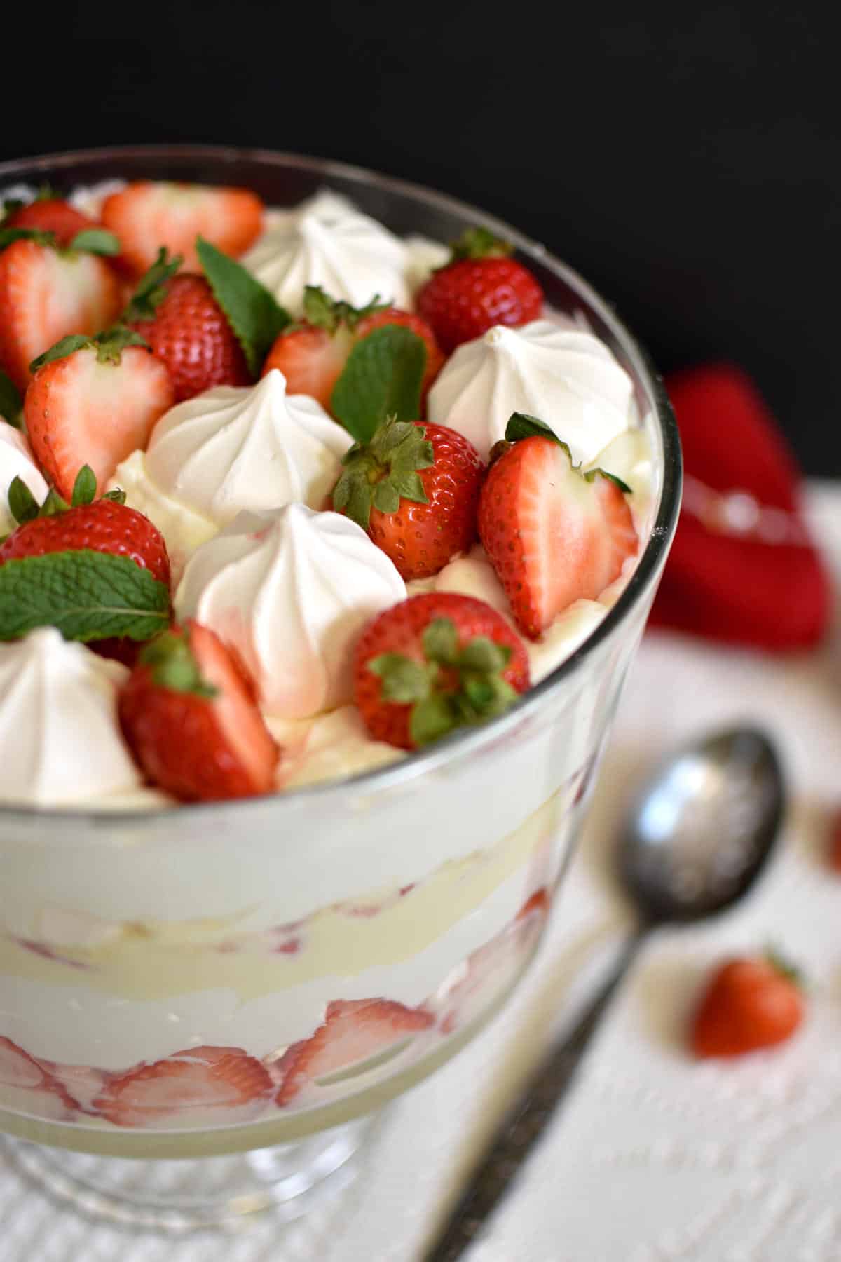 Strawberry trifle in a trifle bowl with strawberries and meringue cookies on top