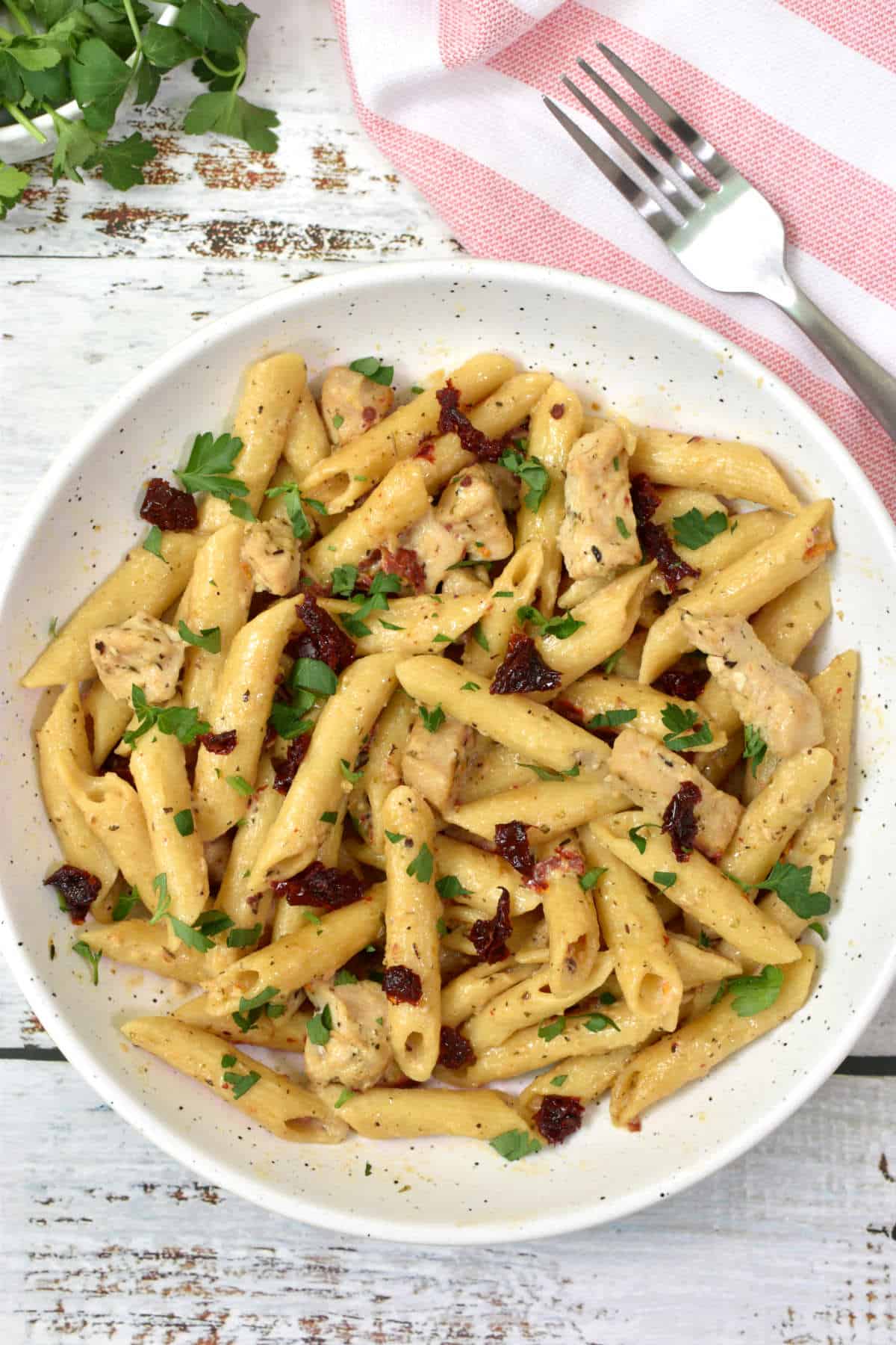 penne pasta with chicken, sundried tomatoes, parsley and parmesan cheese in a plate