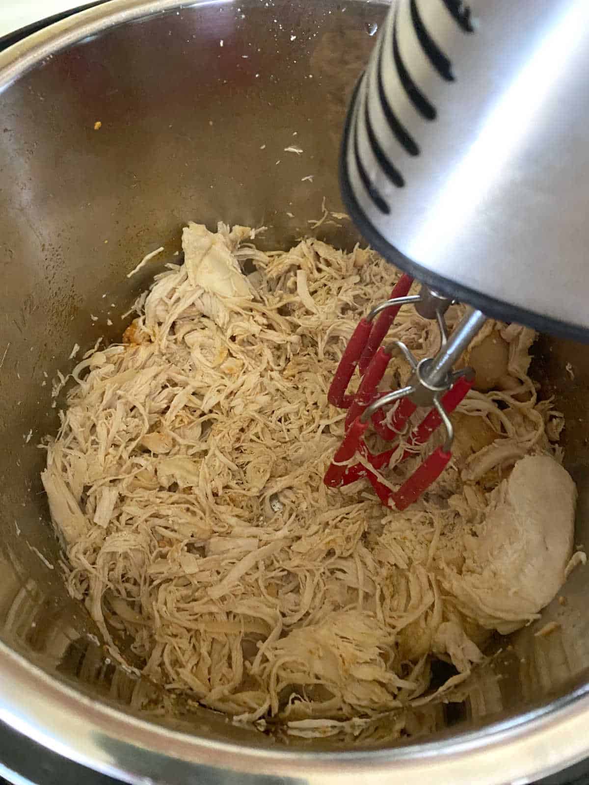 chicken breasts being shredded with a handheld mixer inside the instant pot