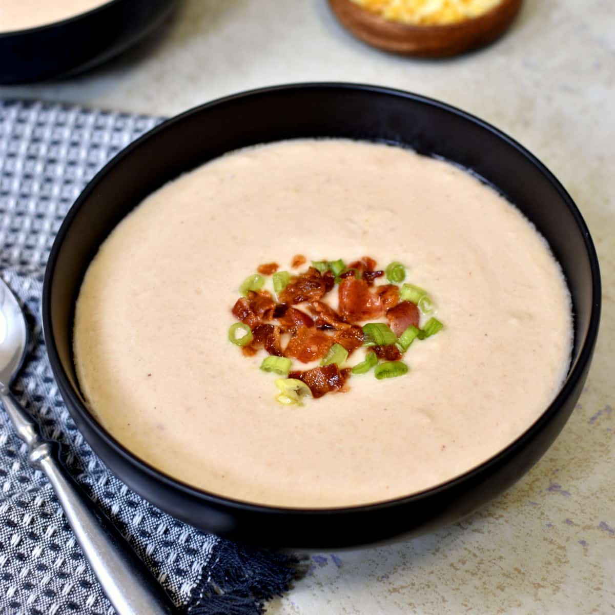 sopa de couveflor em uma tigela preta com bacon e cebolinha por cima