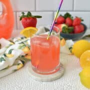 homemade strawberry lemonade in a cup with a straw, ice cubes and garnish