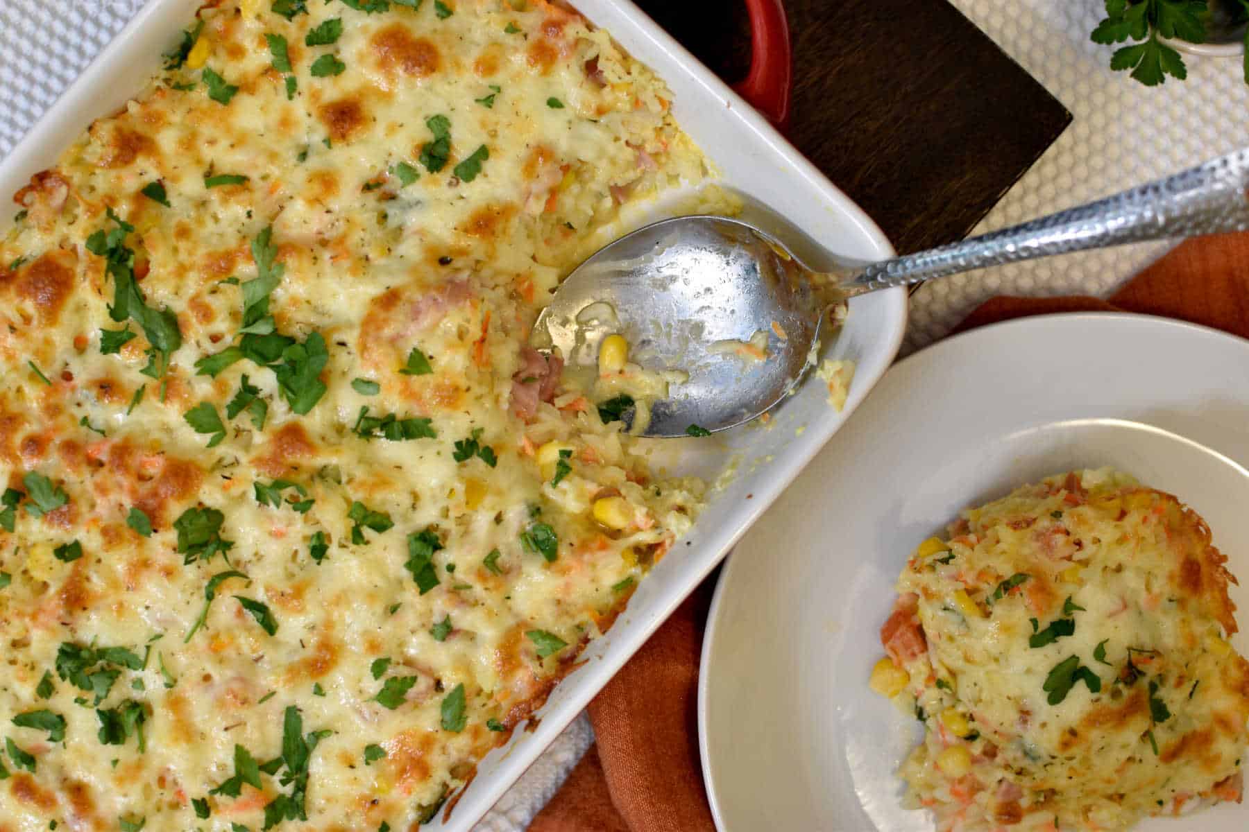 creamy rice casserole with cheese, ham and vegetables with a plate with the rice on the side 