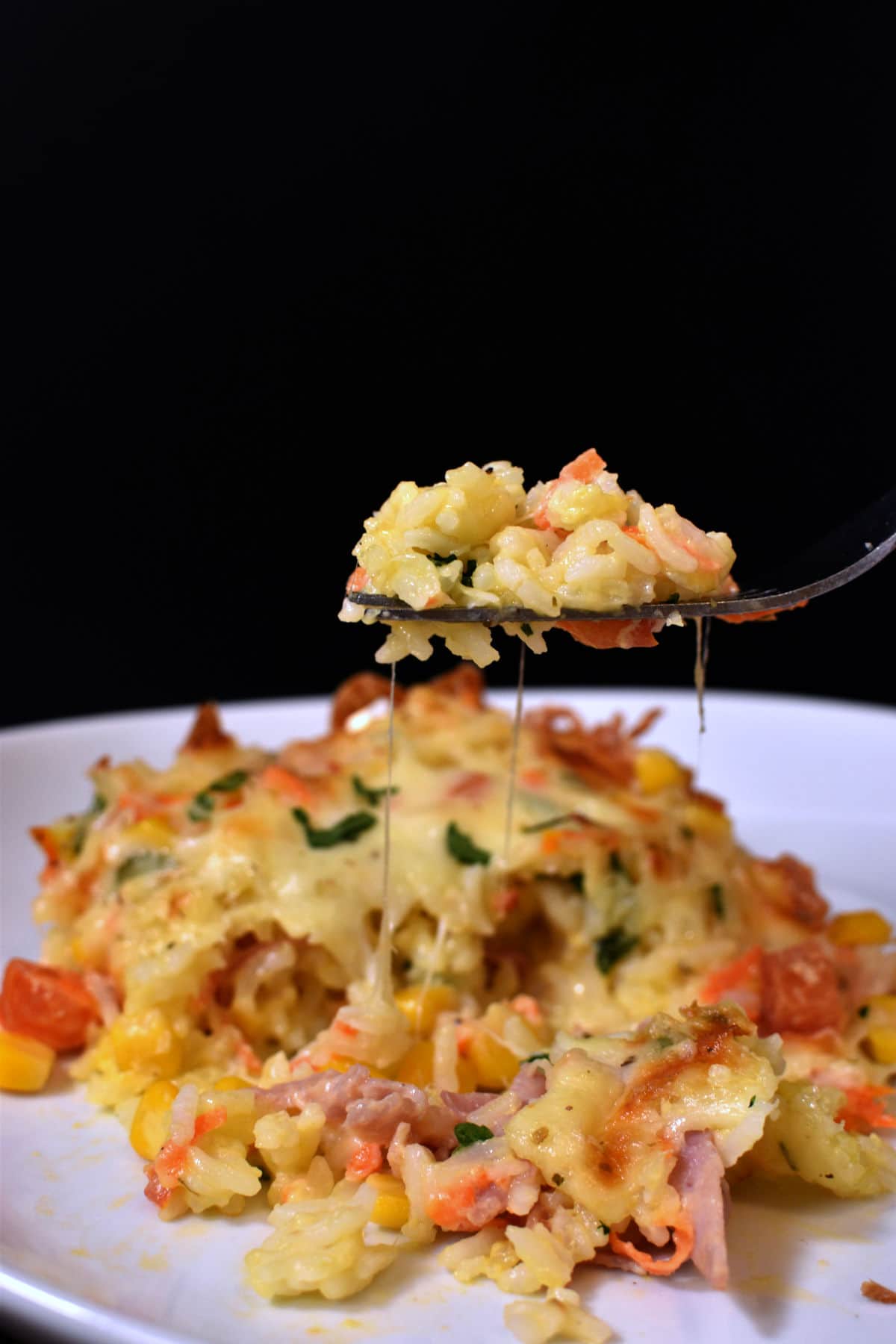 fork holding creamy rice with ham, cheese and vegetables from a plate 