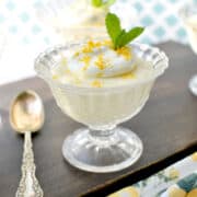 lemon pudding made from scratch in glass cup, topped with whipped cream, lemon zest, and mint leaf.