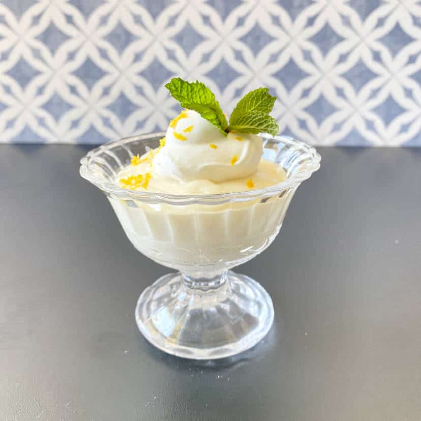 lemon pudding decorated with whipped cream, lemon zest, and mint leaves.