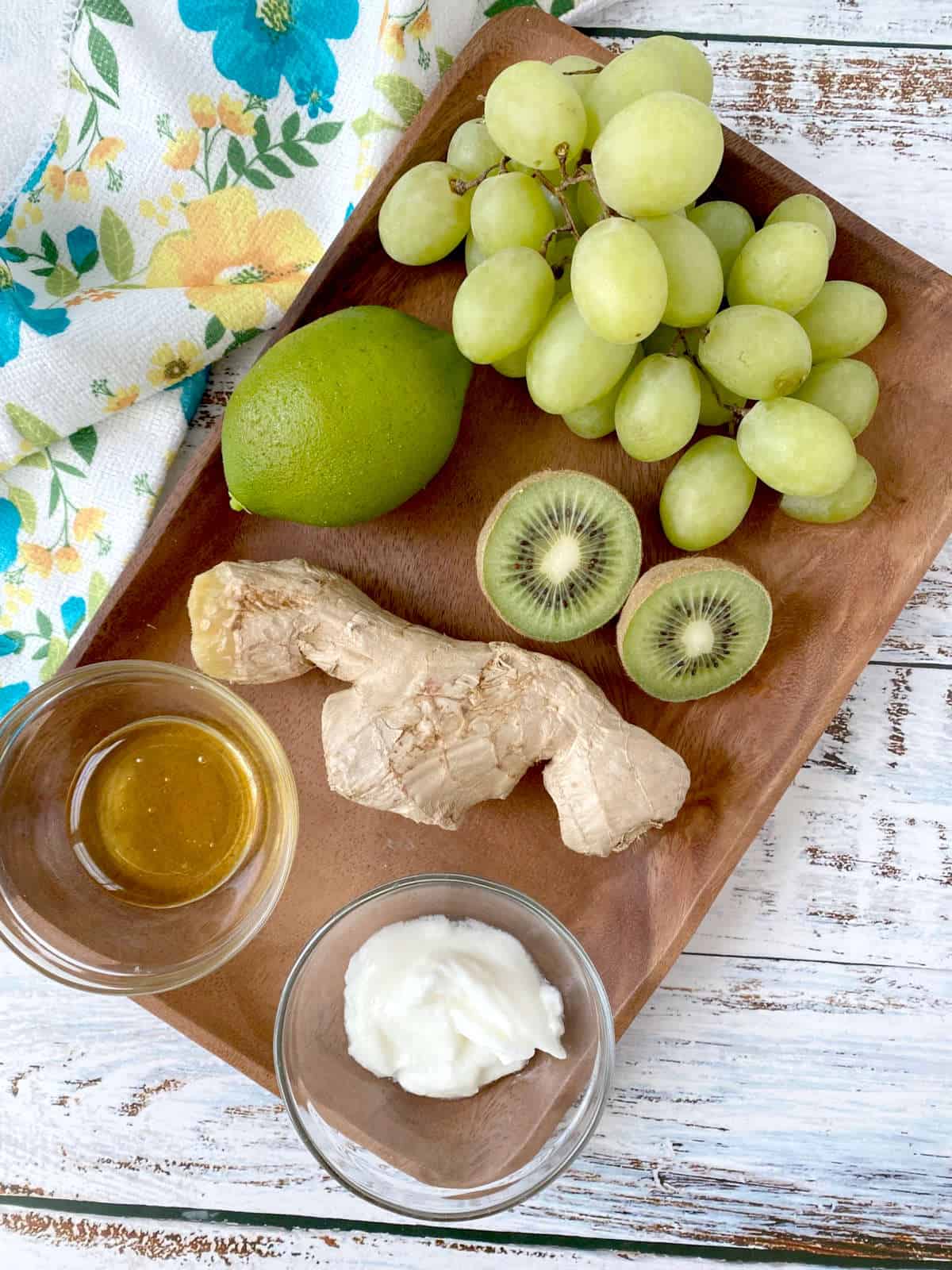 grapes, lime, kiwi, ginger, honey and yogurt on a wood tray.