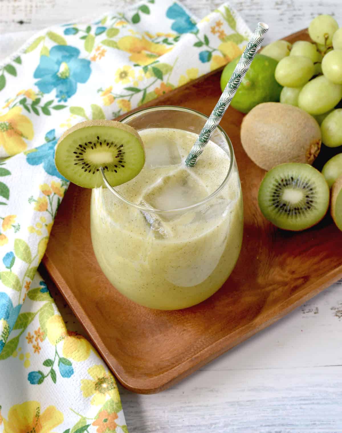 immune system booster smoothie in a cup on a tray with grapes, kiwi and lime on the side.