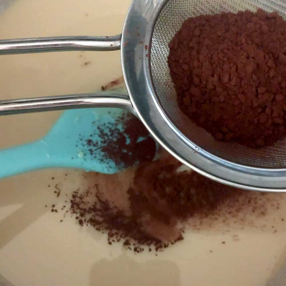 Sifting cocoa powder into sweetened condensed milk in a pan.