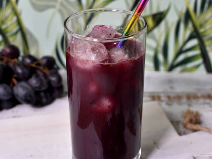 grape juice in a cup with paper straw and ice cubes.