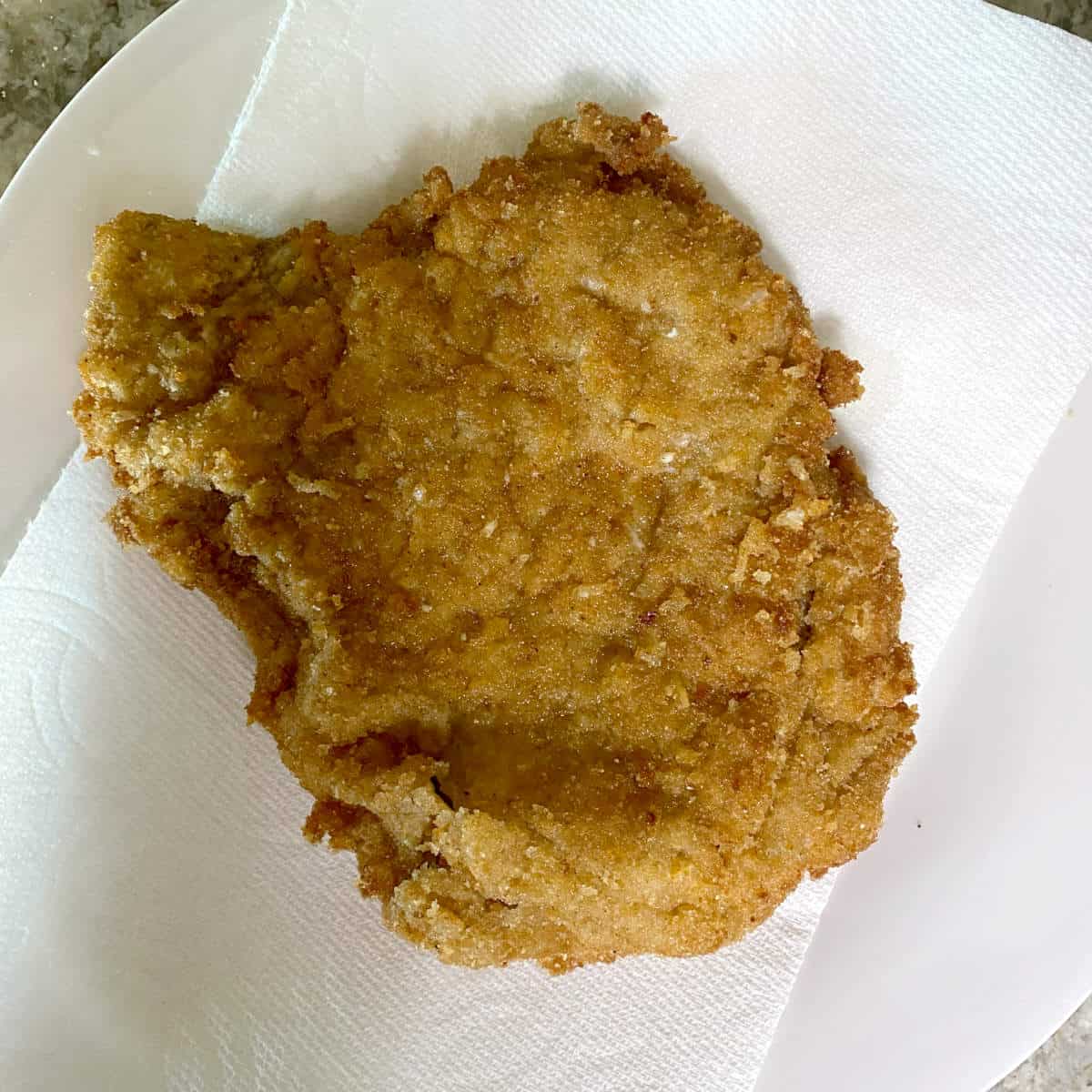 Beef Milanesa sitting on paper towel to dry excess oil.