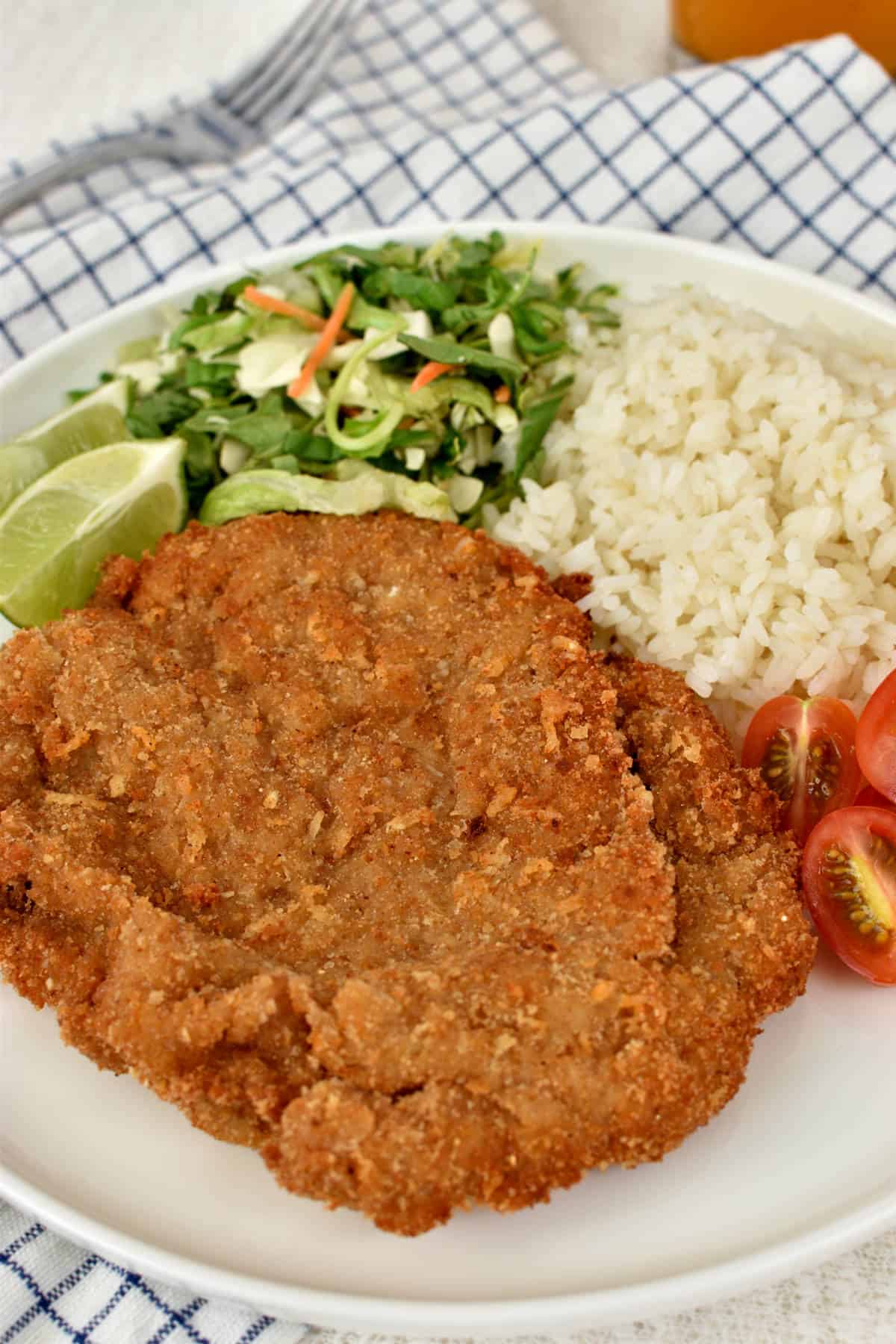 Milanesa steak in a plate with rice, tomatoes, salad, and lime wedges.