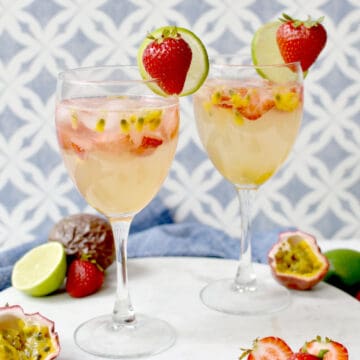 Marble tray with two cups of passion fruit drink mocktail, garnished with a strawberry and lime wheel each, and some strawberries, limes, and passion fruits decorating the tray.