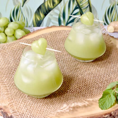 two cups of green grape juice on a wood tray, with ice and garnished with a little heart made of grape.