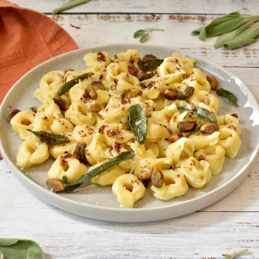 Plate with tortellini, topped with butter sauce, sage, and pistachios.