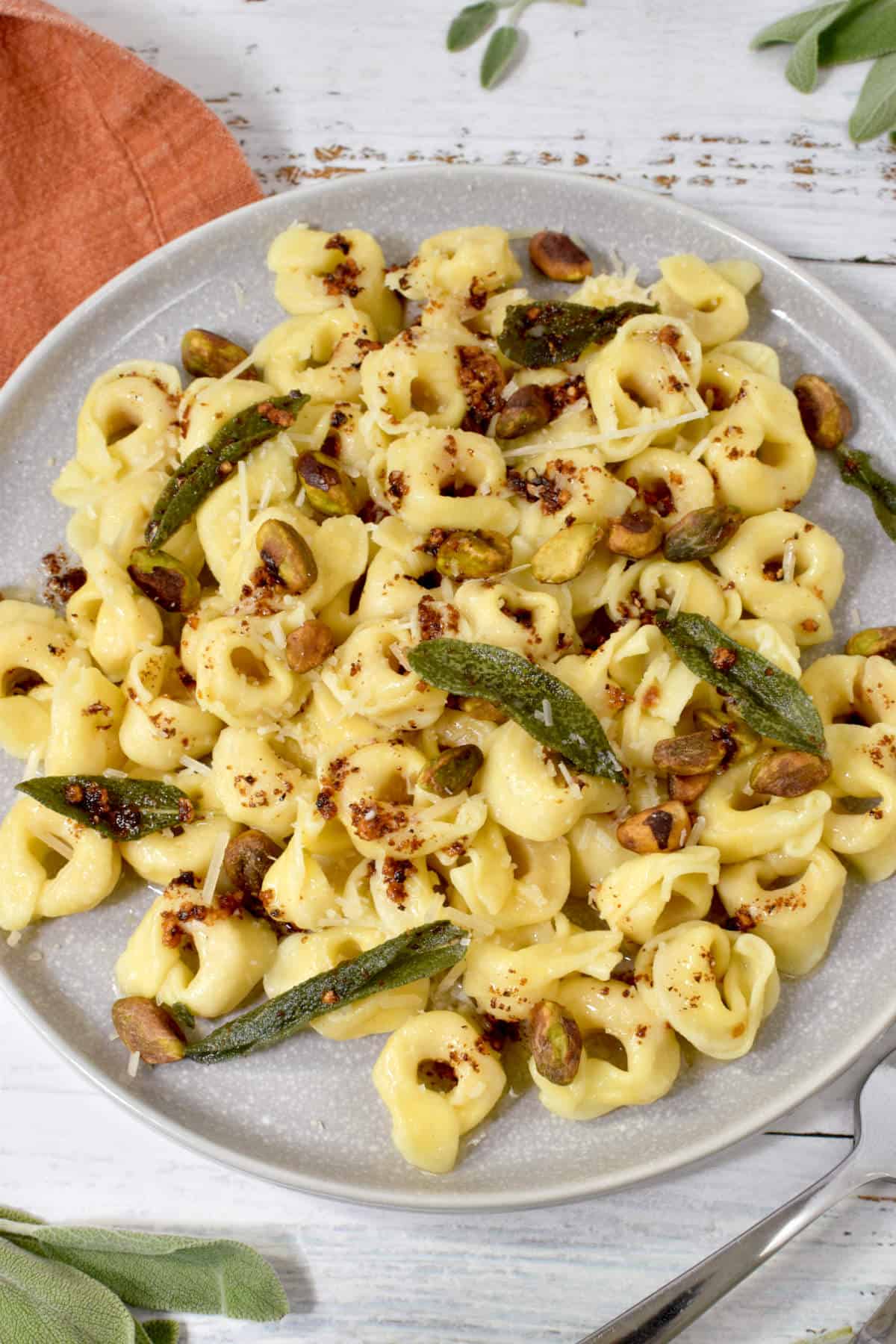 tortellini in a plate with butter sauce, sage, parmesan, and pistachios.