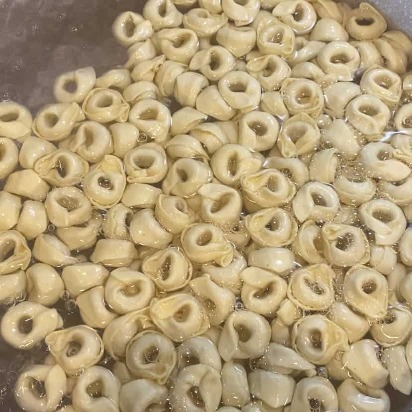 cheese tortellini being cooked in a pot of boiling water.