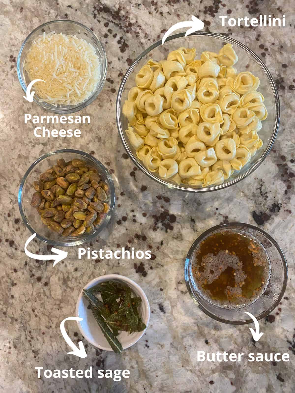 ingredients for the butter sauce tortellini on a counter: cheese tortellini, parmesan cheese, pistachios, toasted sage leaves, and butter sauce.